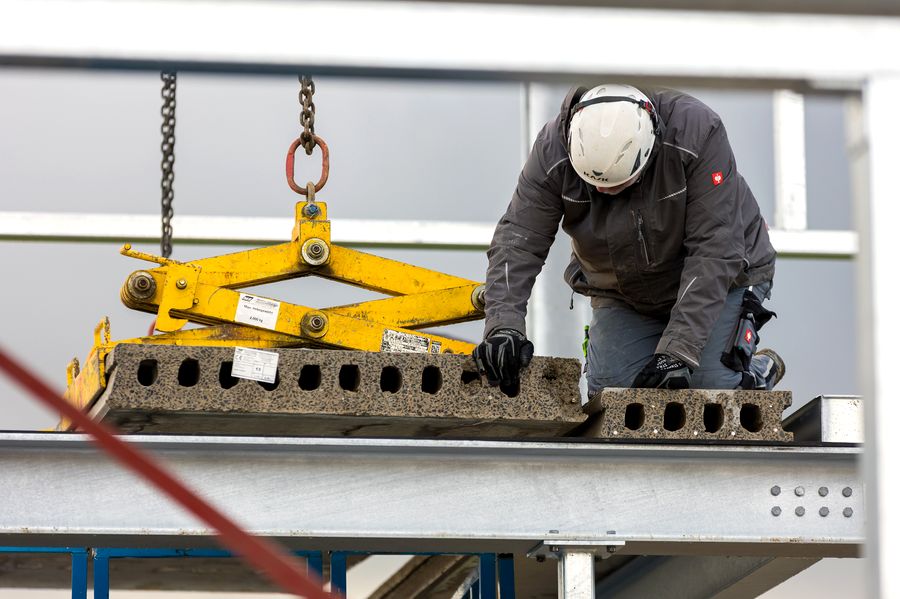 Arbeiter verlegt Betonfertigteildecke mit gelbem Krangeschirr